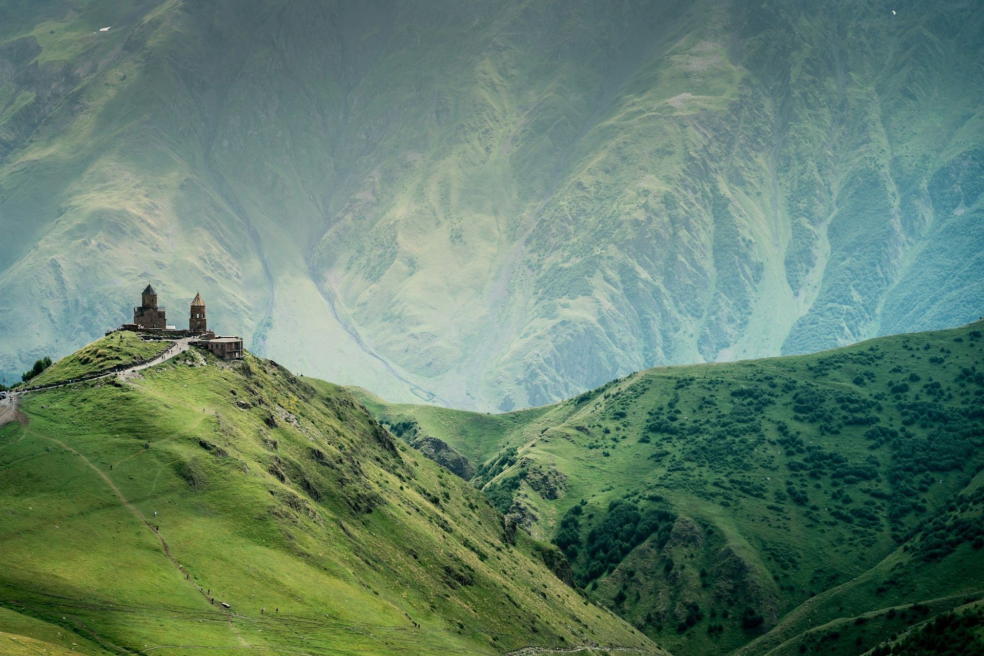 Stone church atop green mountain ridge, overlooking a vast mountainous landscape.