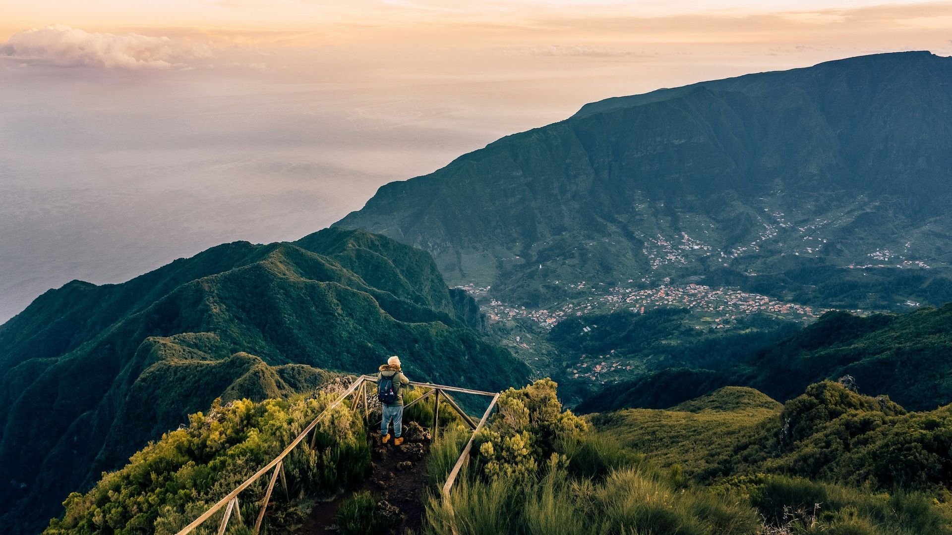Person hiking on a mountain ridge, looking at a valley and coastal view.
