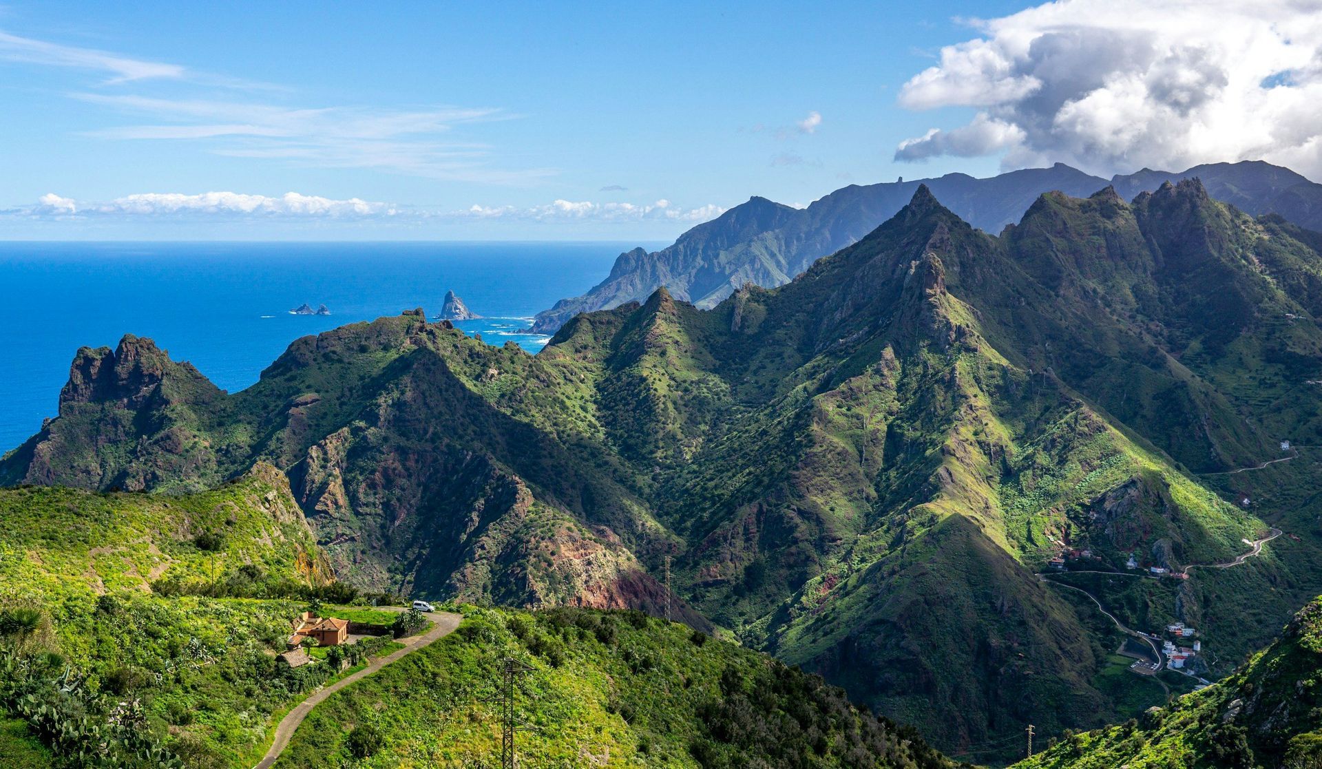 Green, mountainous landscape meeting a blue ocean under a bright sky.