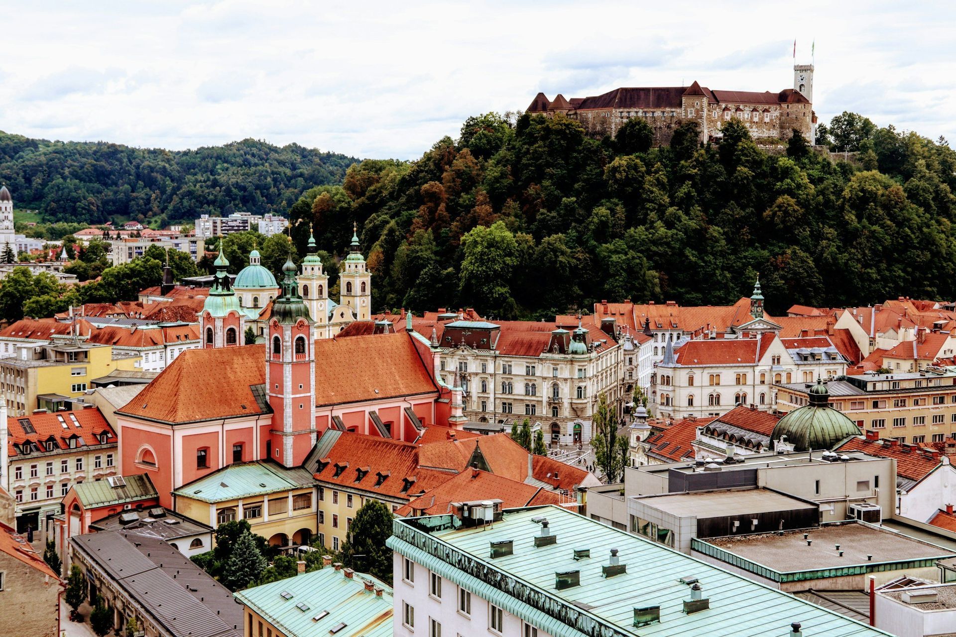 Ljubljana, Slovenia cityscape with red-tiled roofs, churches, and Ljubljana Castle atop a hill.