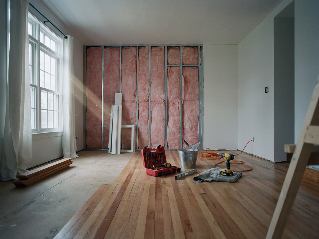 Renovated living room with exposed insulation, bare floorboards, tools, and scattered construction materials