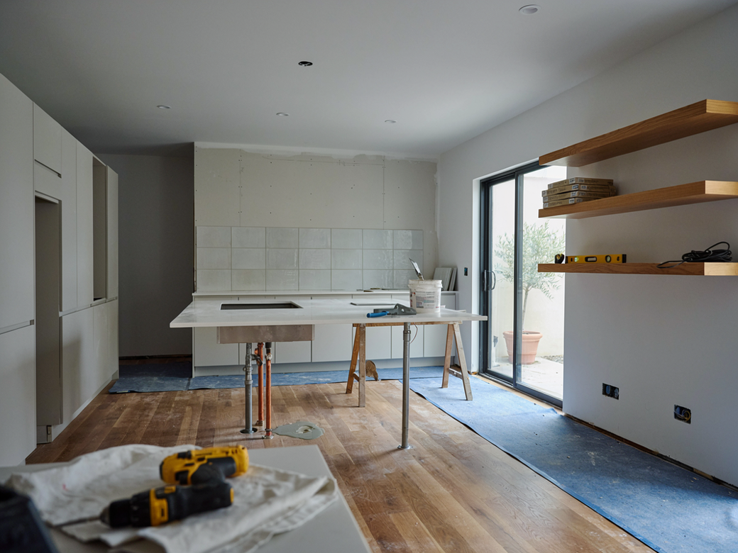Unfinished modern kitchen with white cabinets, island, wood floor, and open shelves by sliding glass doors