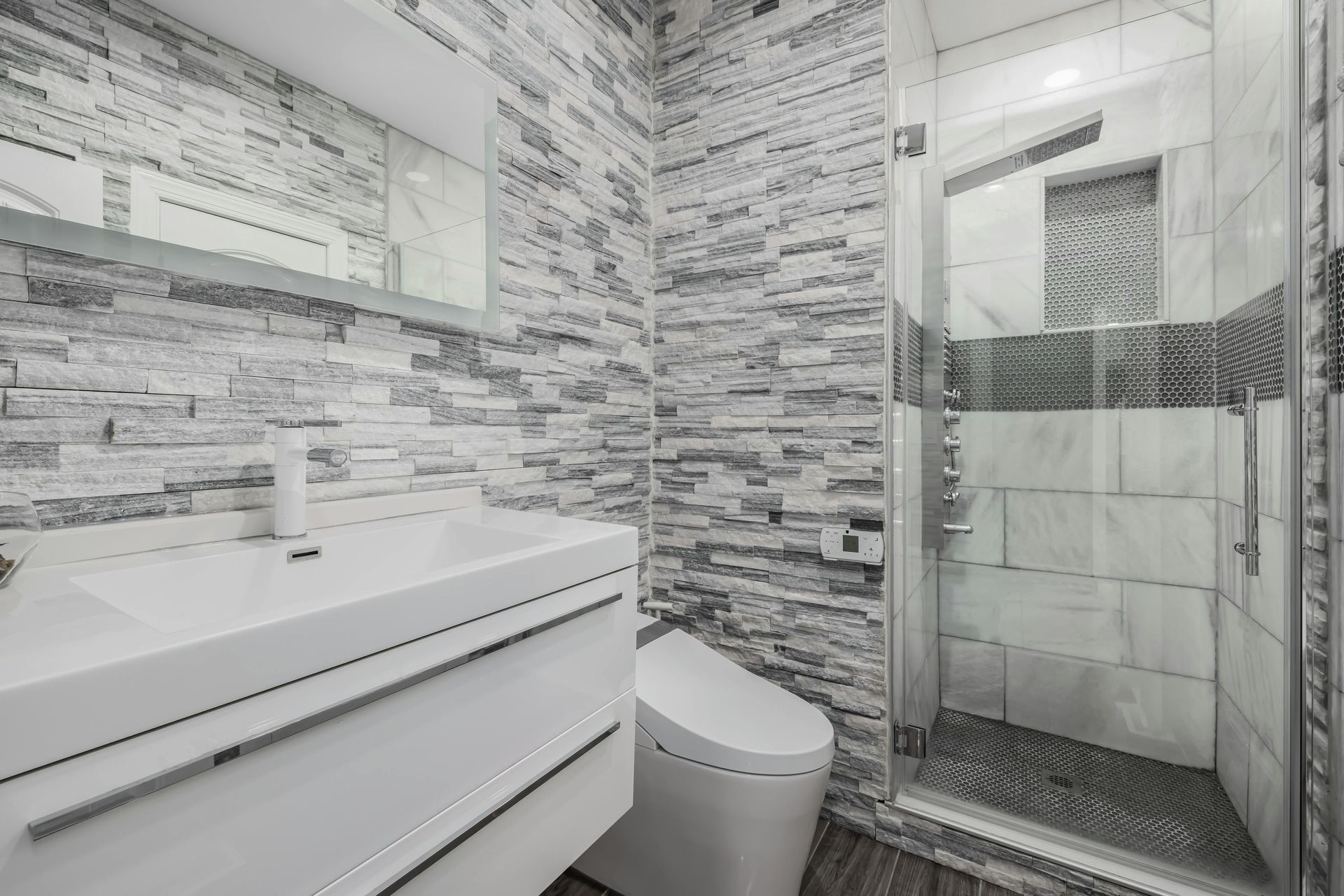Modern bathroom with white vanity, toilet, and glass shower with gray tile walls