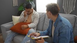 Two people on a sofa; one looks upset while the other offers support with a notepad.