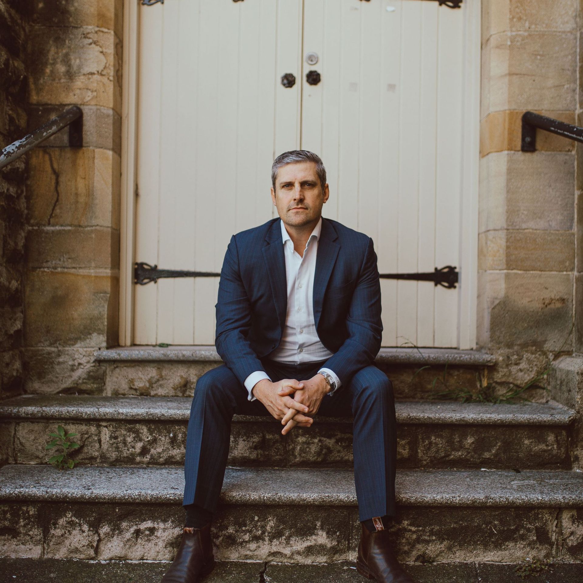 A man in a suit is sitting on the steps of a building.
