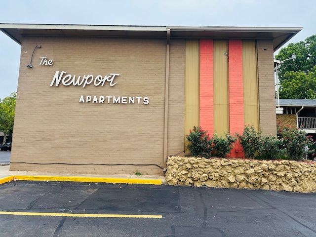 The Newport Apartments building with tan facade, orange and gold accent, and green bushes.
