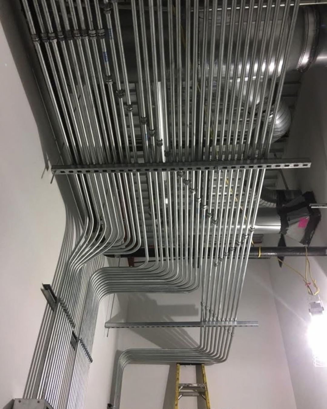 Rows of silver metal pipes and conduits running along a ceiling in a utility room
