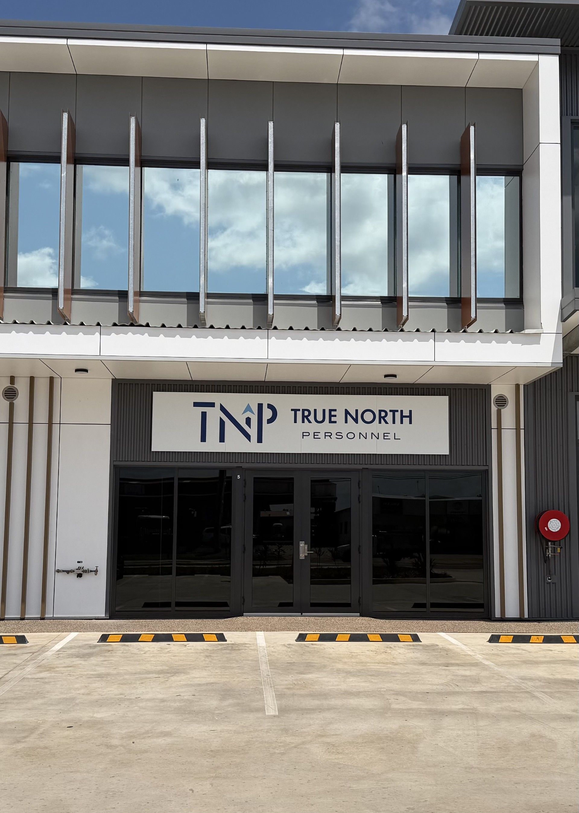 Exterior of the True North building with a glass entrance and white facade, viewed from the parking area
