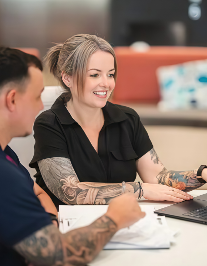 Two coworkers talking at a table with a laptop in a modern office lounge