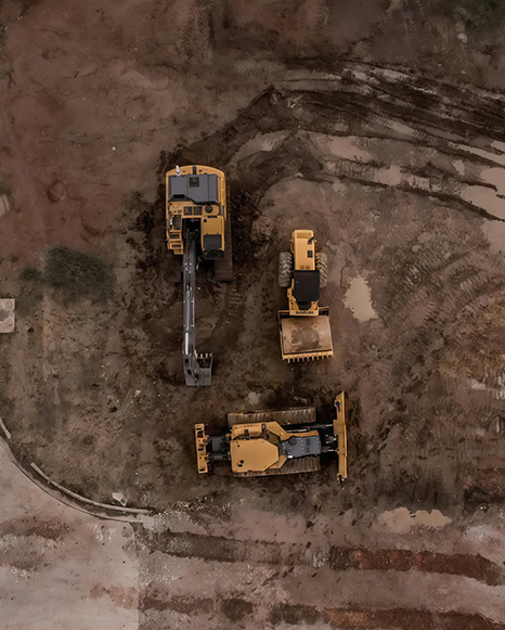 Three yellow construction vehicles on a dirt worksite, viewed from above.