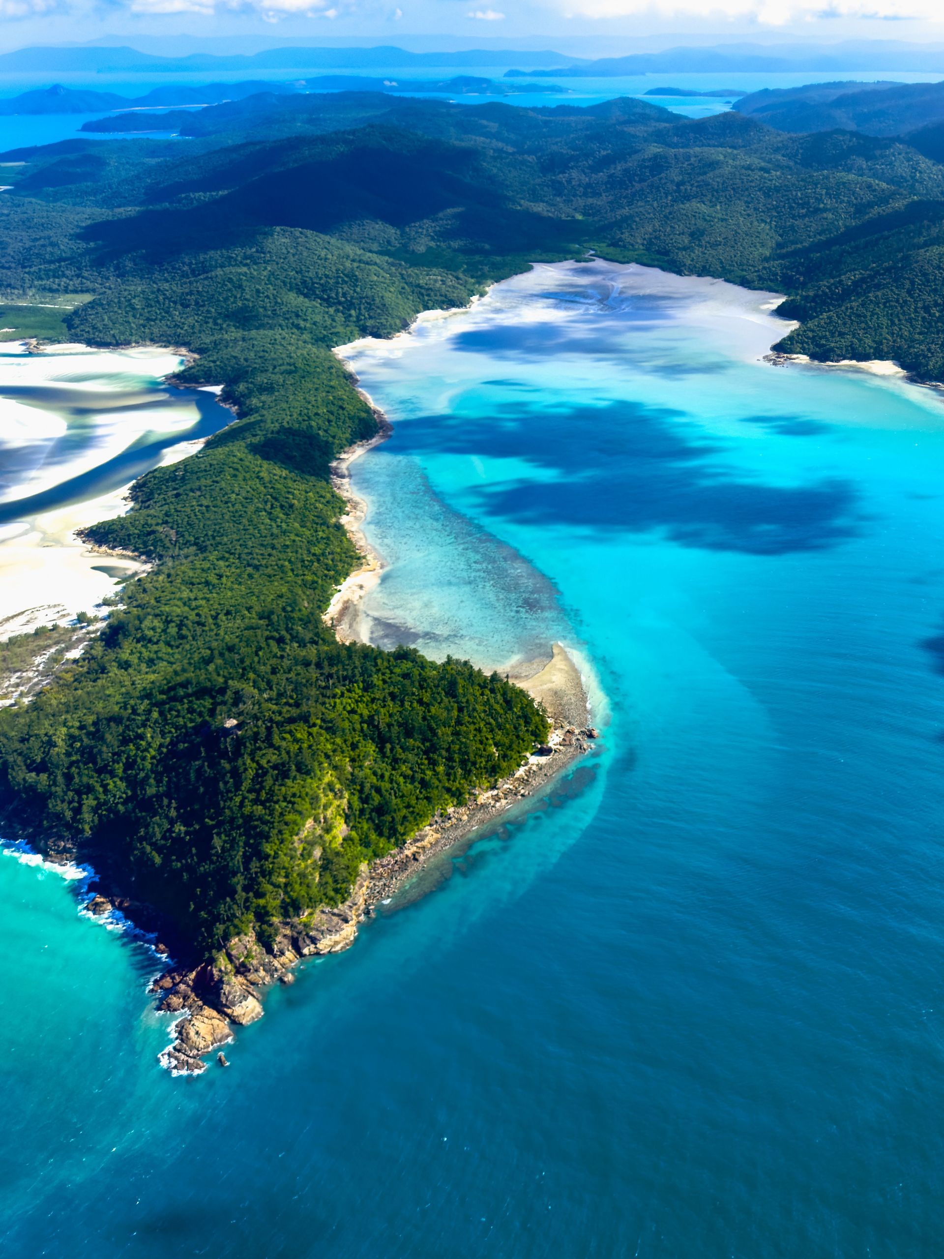 Aerial view of a tropical island with white sand beaches, turquoise water, and lush green forest.