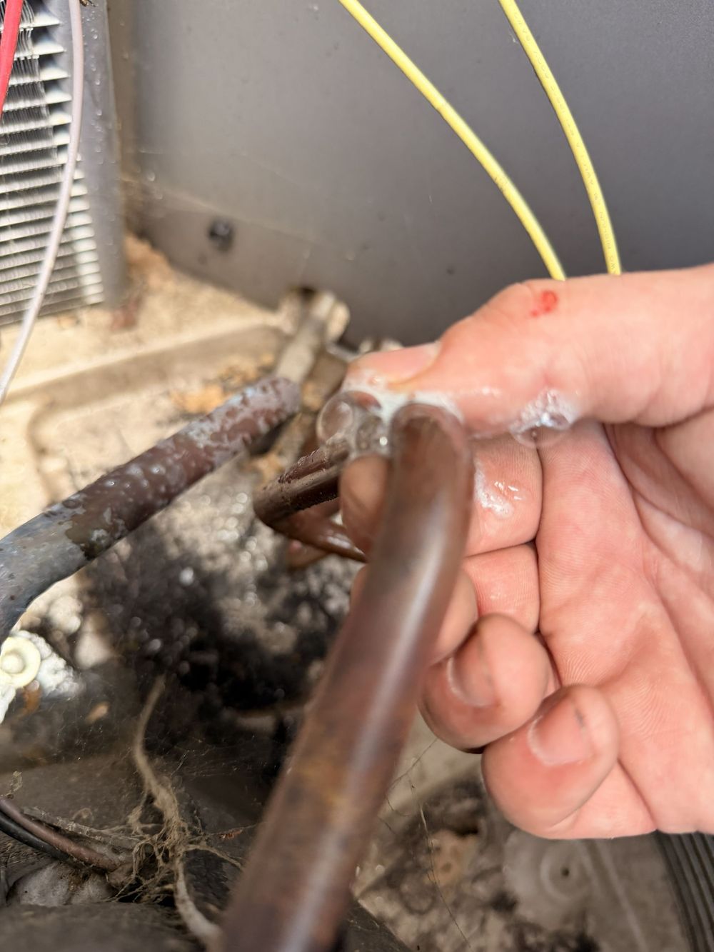 Technician connecting white refrigerant hoses to an outdoor AC unit with blue and yellow lines nearby