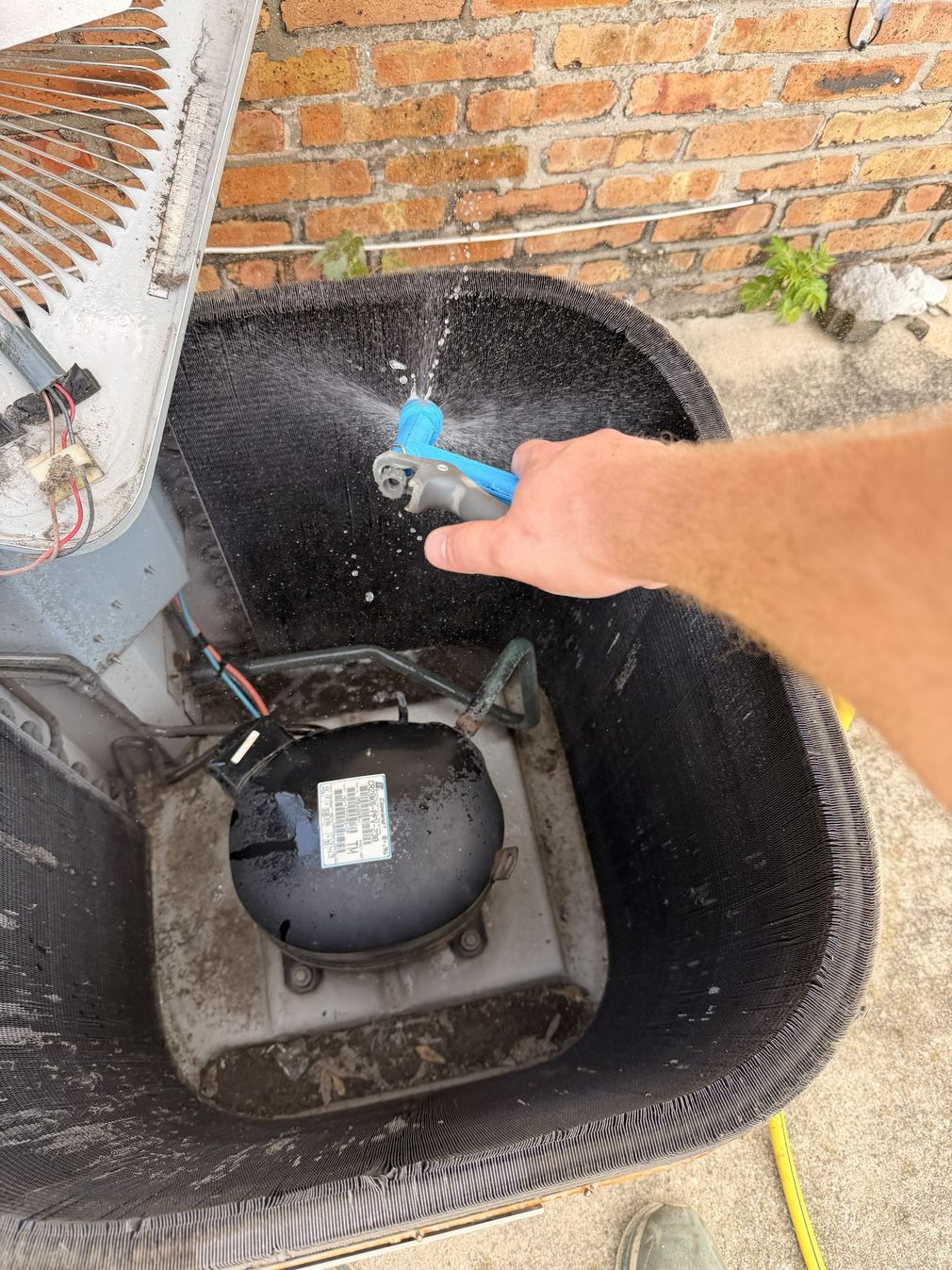 Technician in blue hard hat checking HVAC gauges on an outdoor unit with red and blue dials