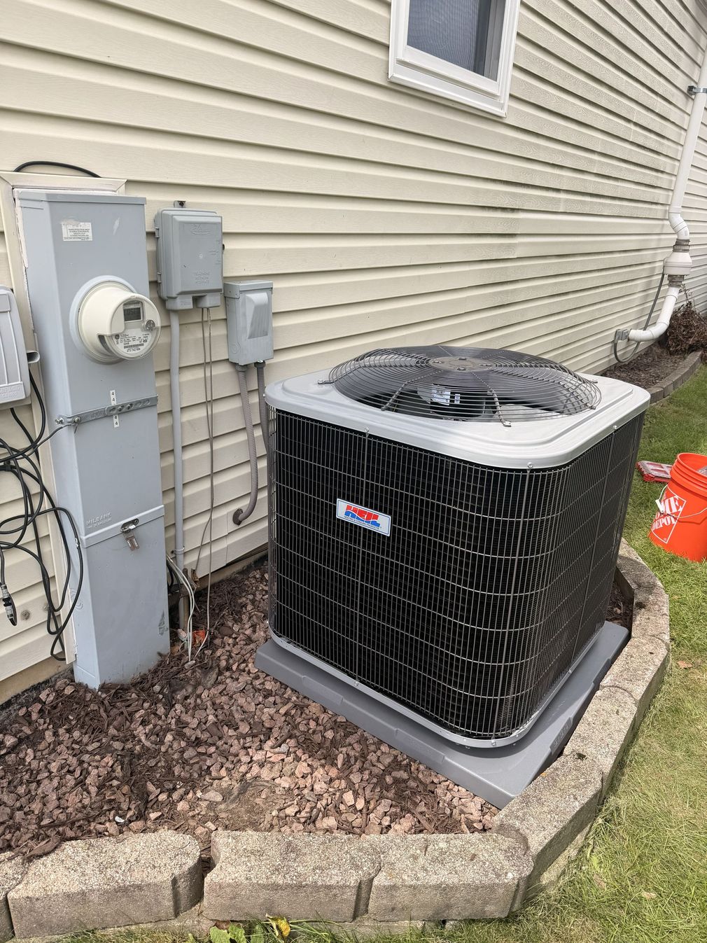 Outdoor HVAC unit beside a brick house, with a grassy lawn and shrubs nearby