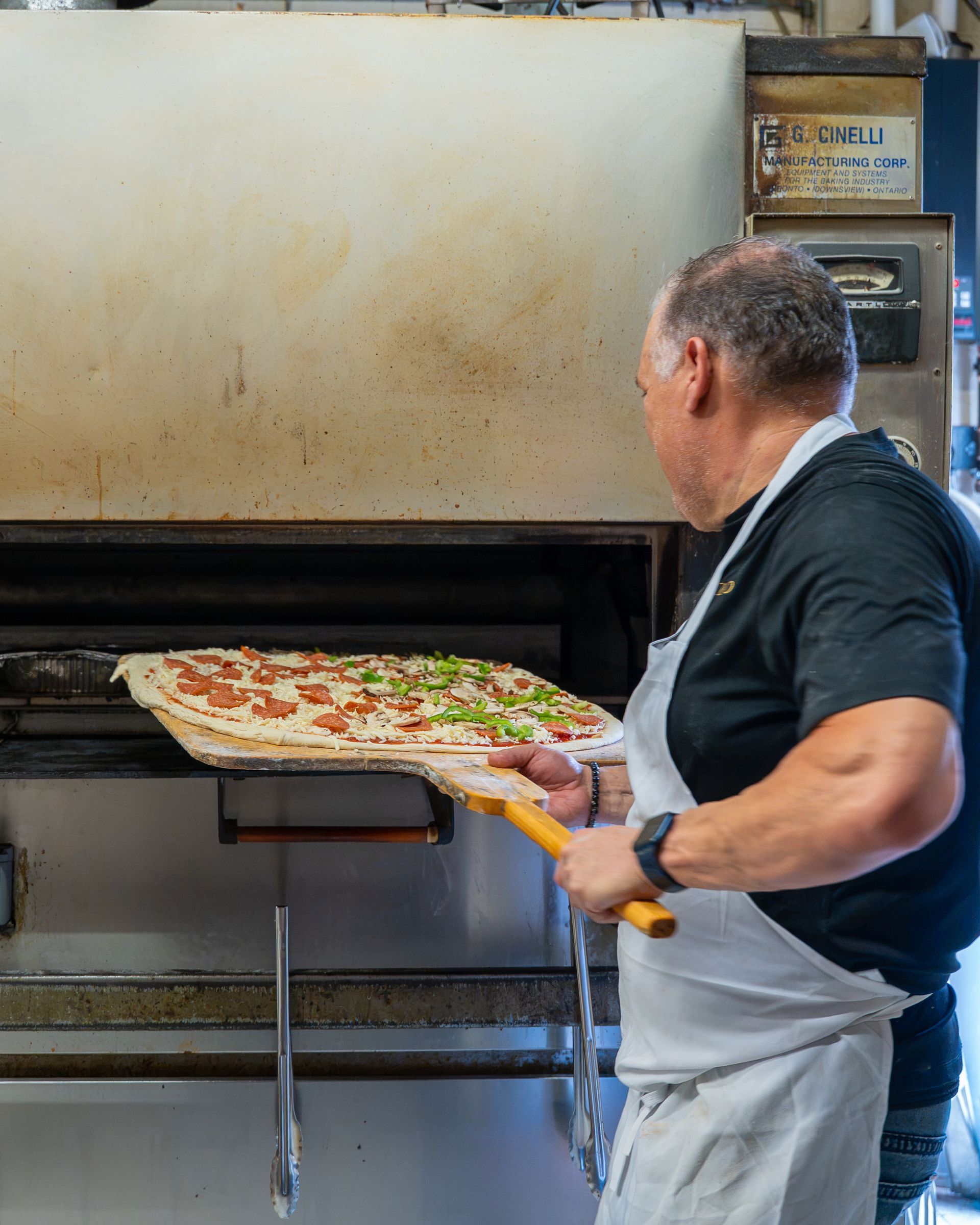 Man sliding a pizza into a large oven in a pizzeria kitchen
