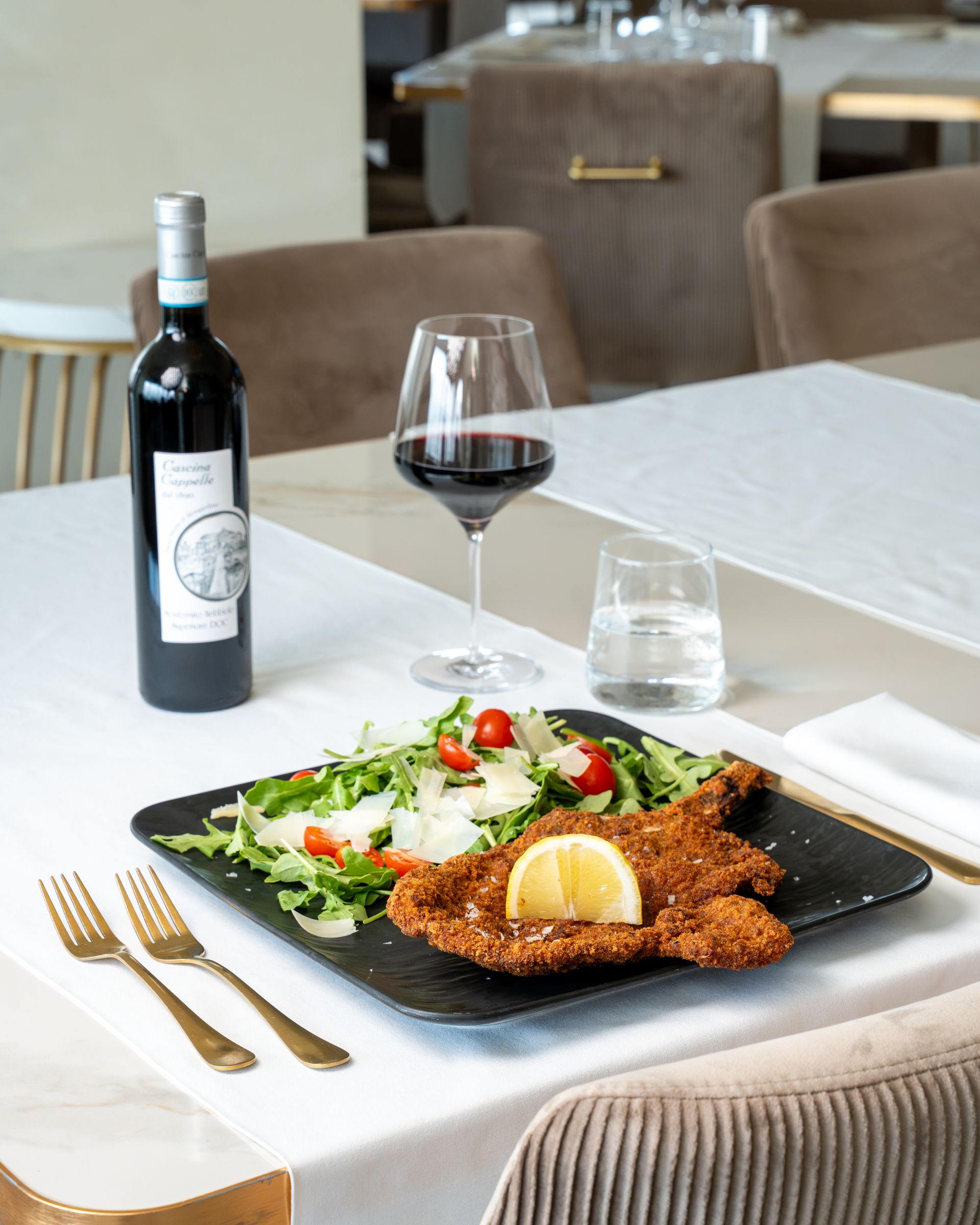 Wine bottle and glass beside a plated meal on a restaurant table with salad and fried entrée.