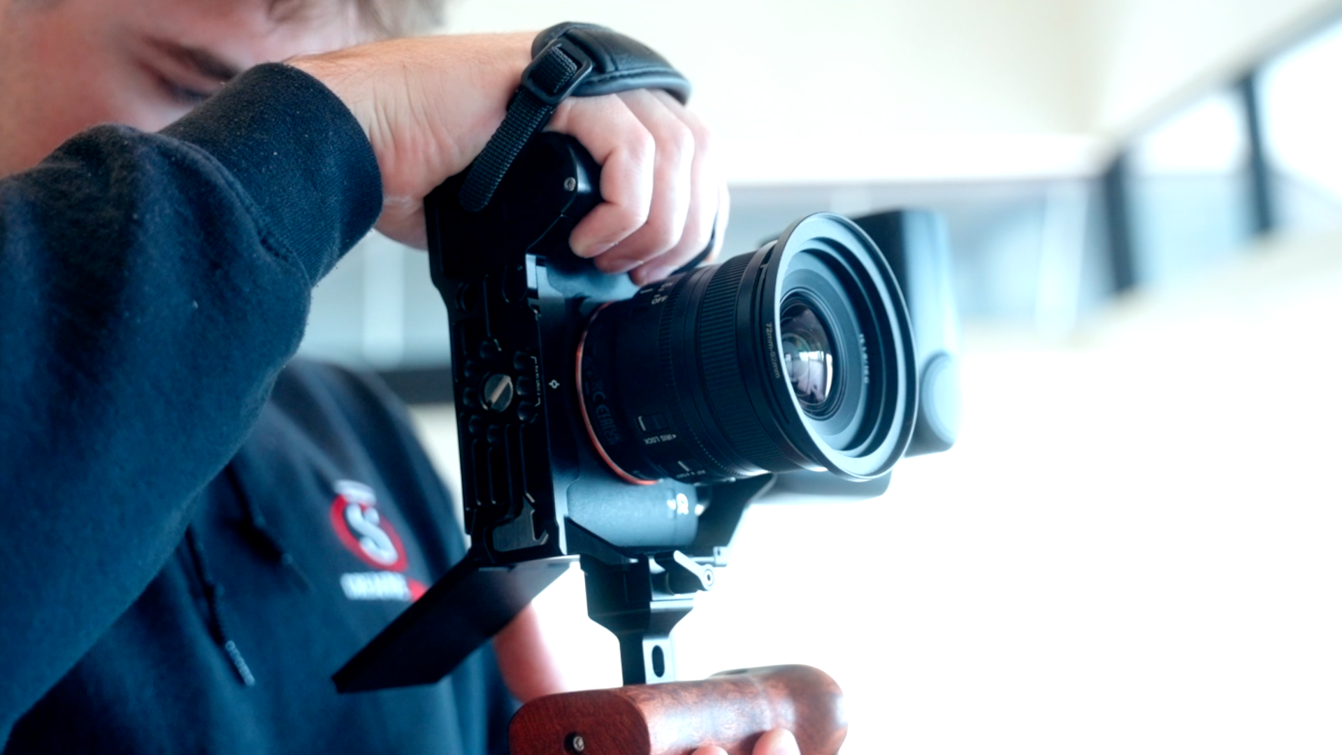 Person holding a DSLR camera with a large lens, aiming it in a bright indoor setting