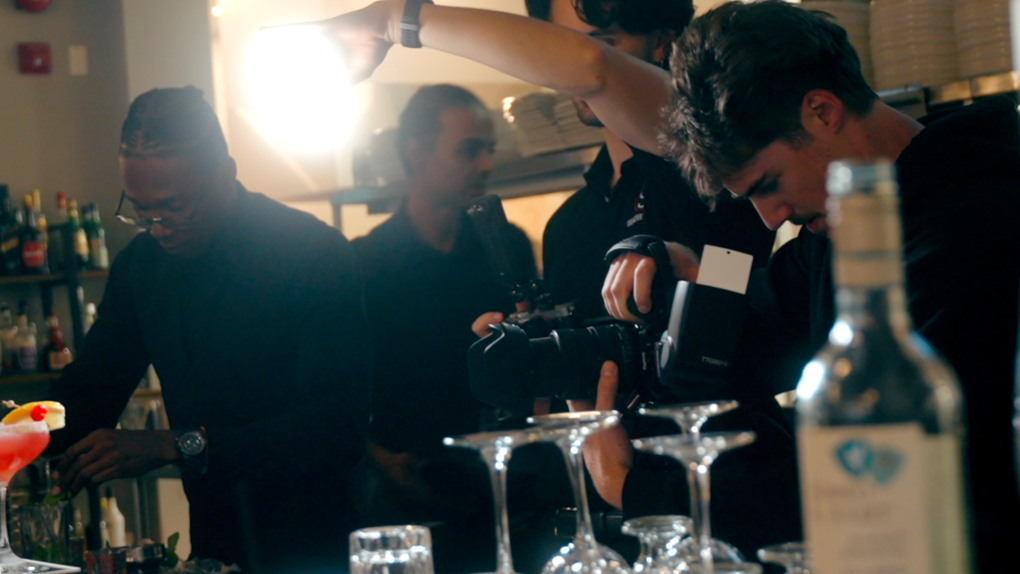 Bartender pouring drinks behind a bar as patrons mingle under warm nightclub lighting.