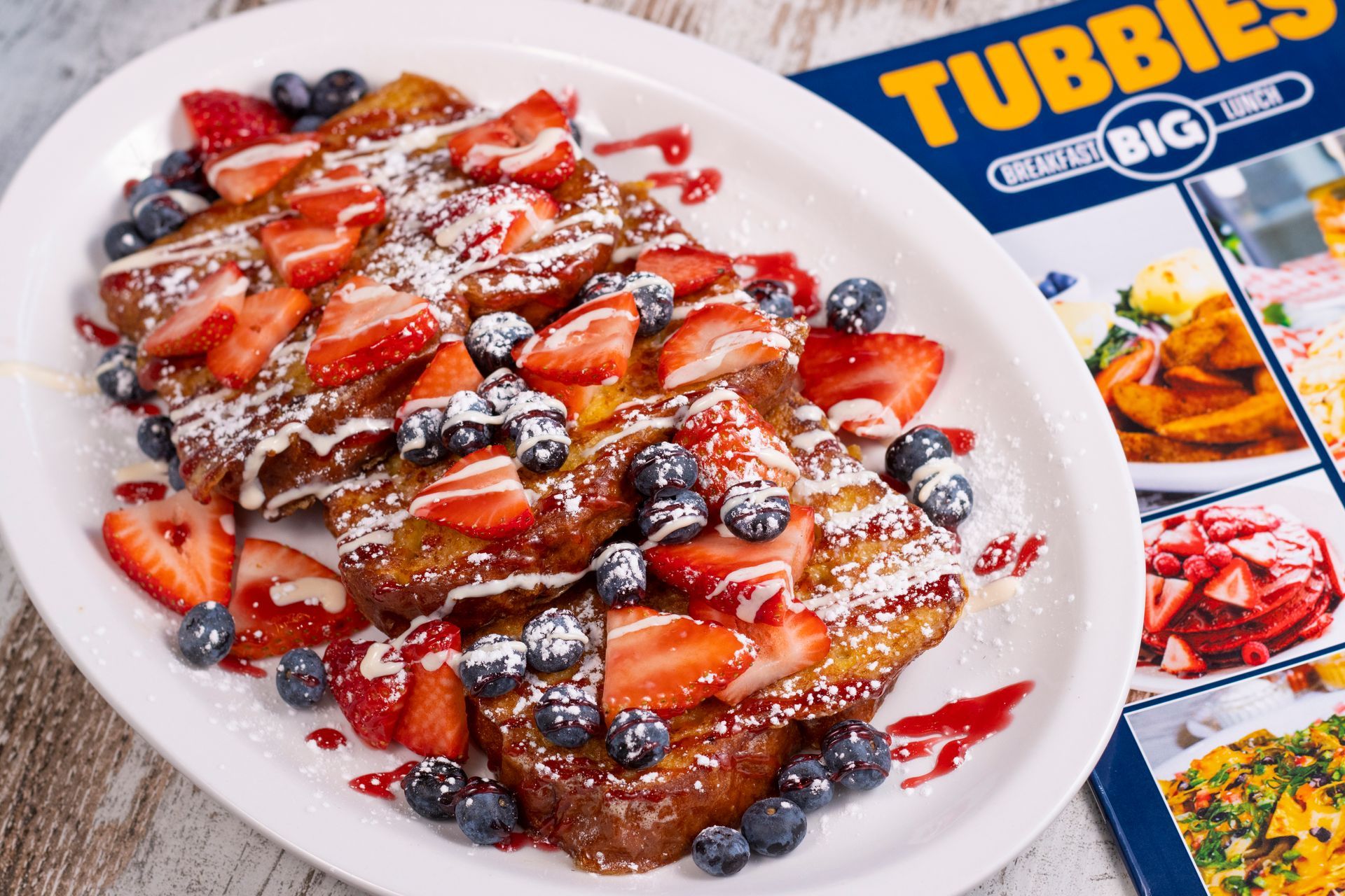 A plate of french toast with strawberries and blueberries next to a menu.