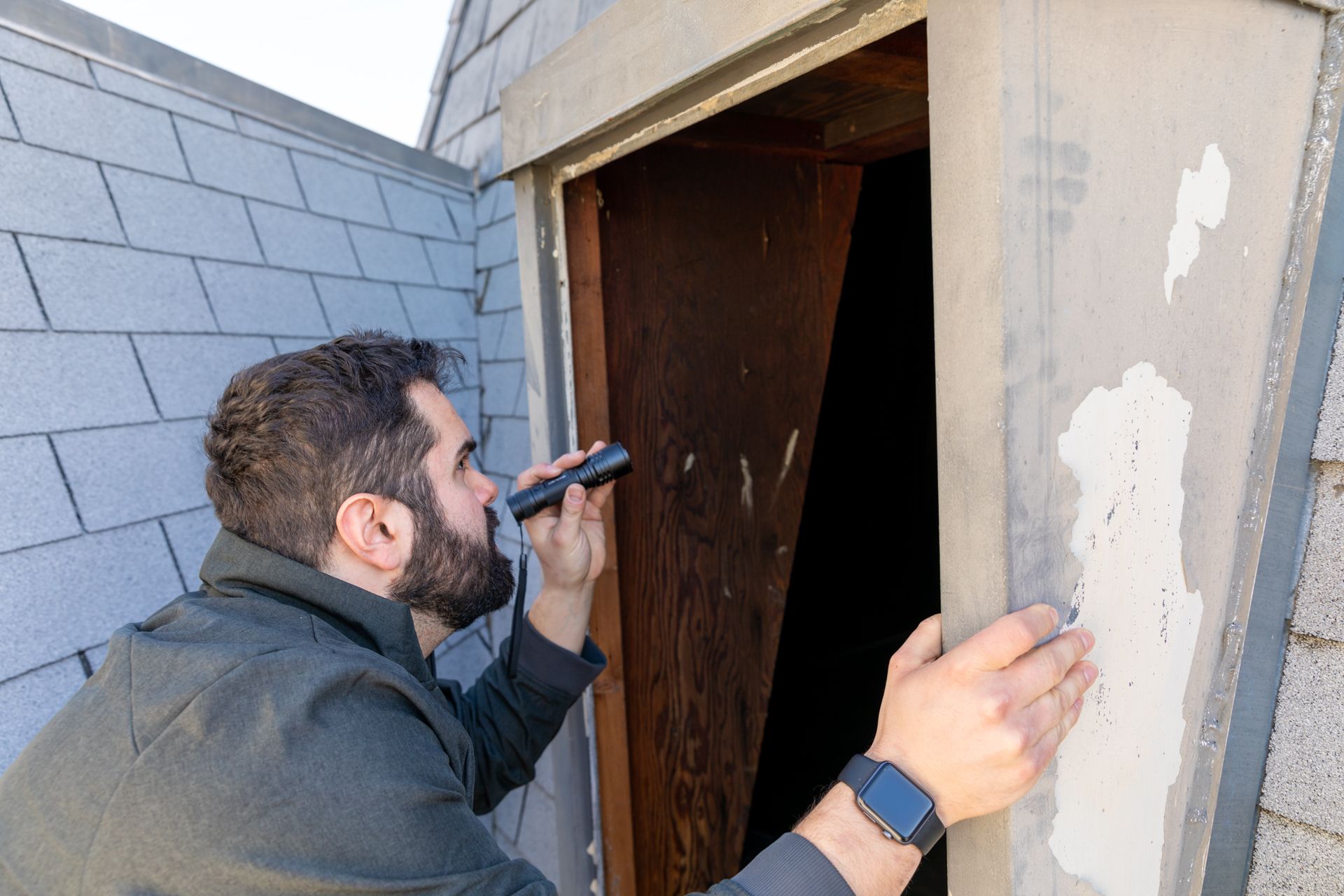 Man using a flashlight to inspect a doorway or wall opening outdoors
