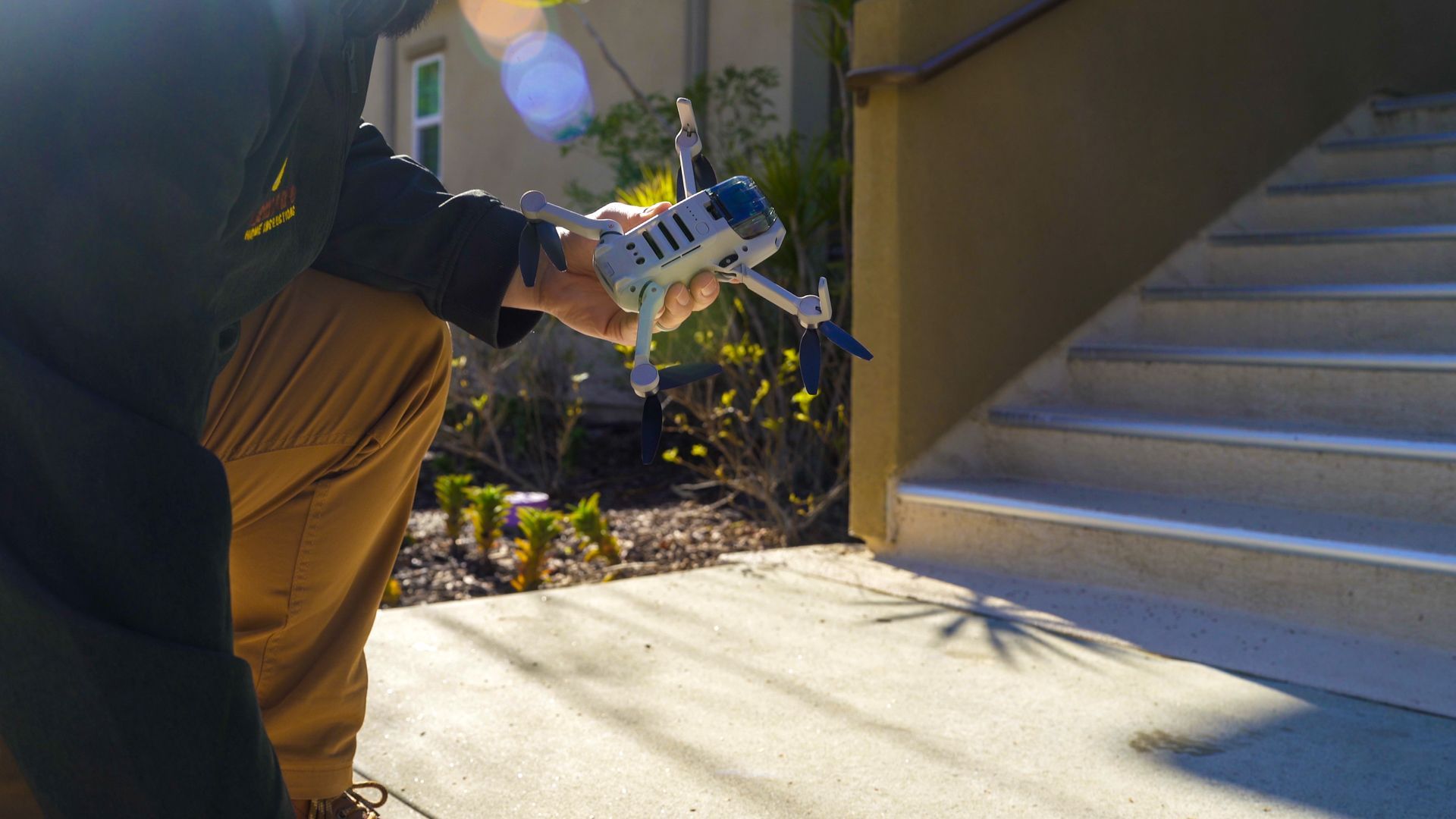 Person flying a drone beside outdoor steps and a home entrance.
