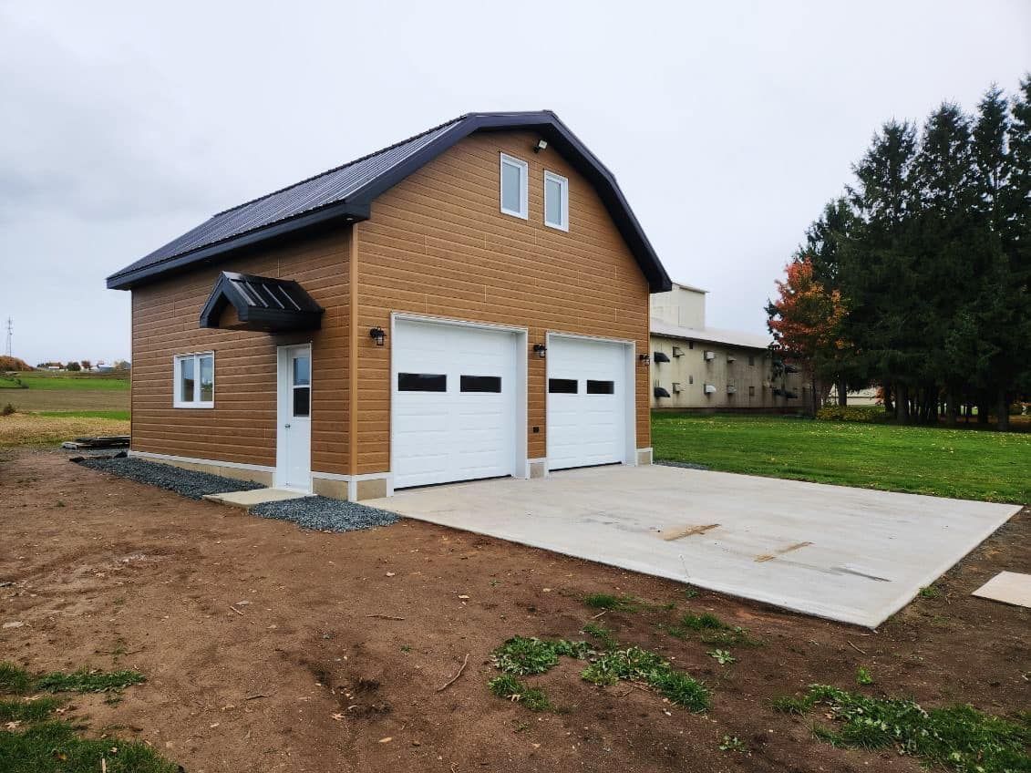 Un garage avec deux portes de garage est assis au milieu d'un champ.