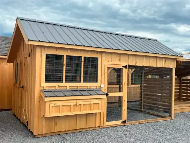 A wooden chicken coop with a metal roof and a chicken run.
