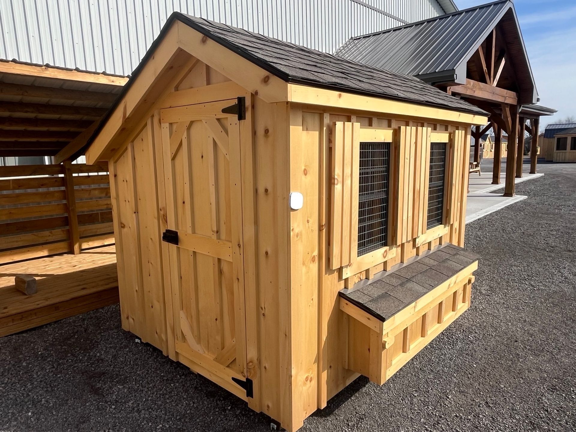 A small wooden chicken coop is sitting in a gravel lot in front of a building.
