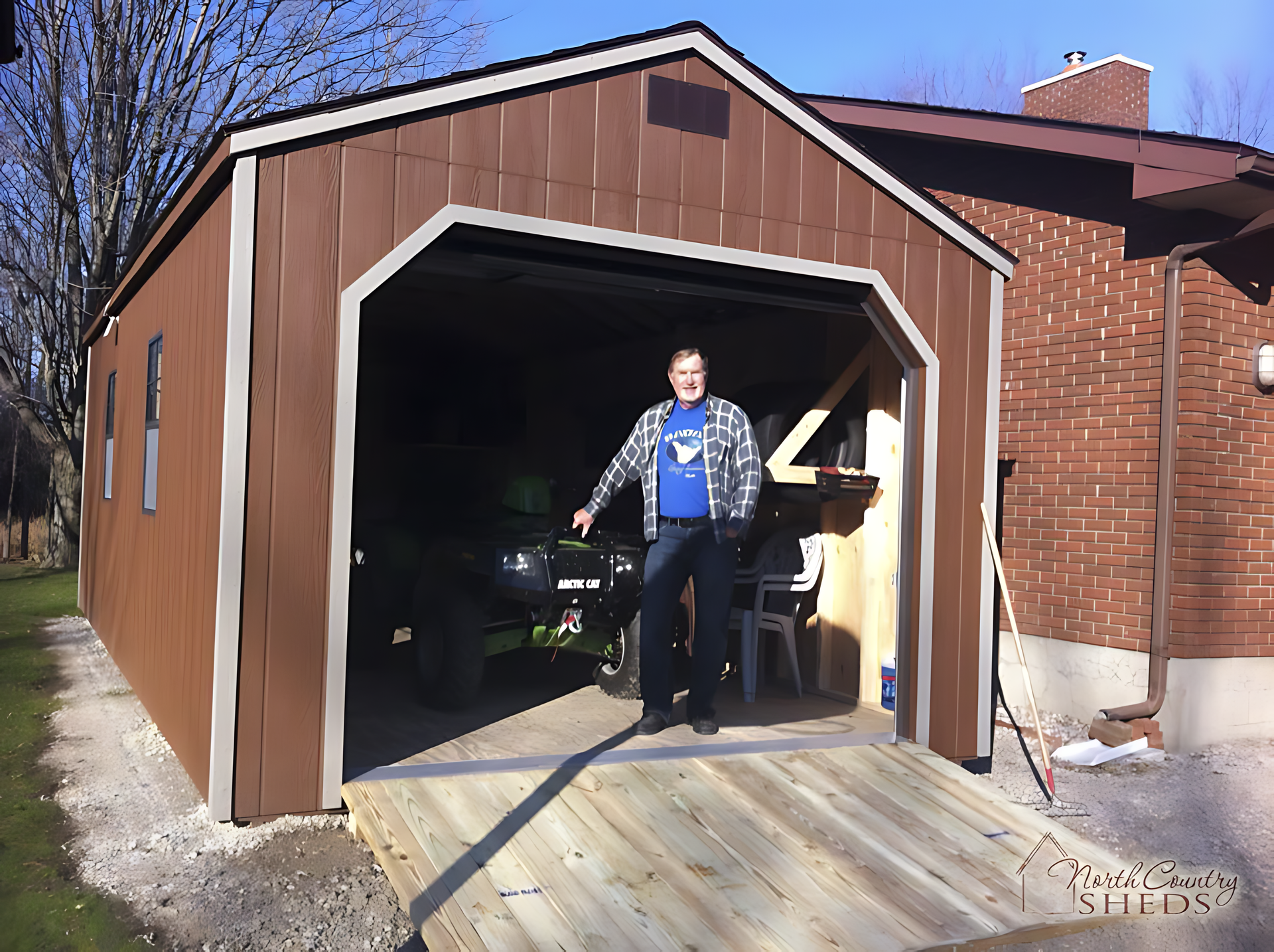 A man in a blue shirt stands in front of a brown garage