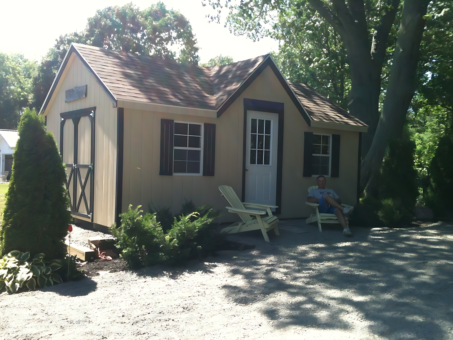 A man sits in a chair in front of a small house