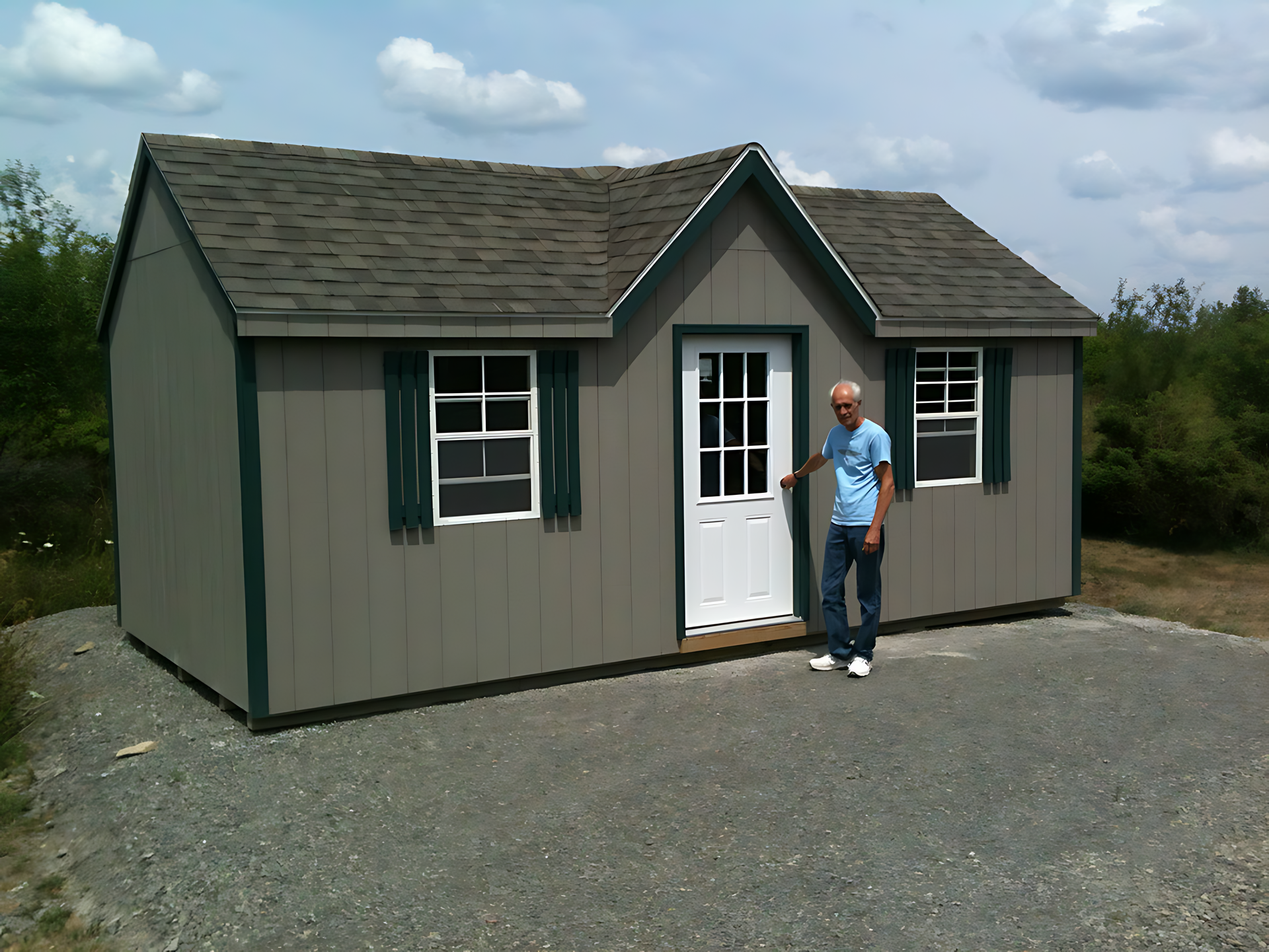 A man in a blue shirt stands in front of a small house