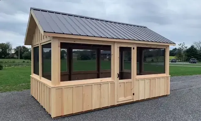 A small wooden gazebo with a screened in porch and a metal roof.
