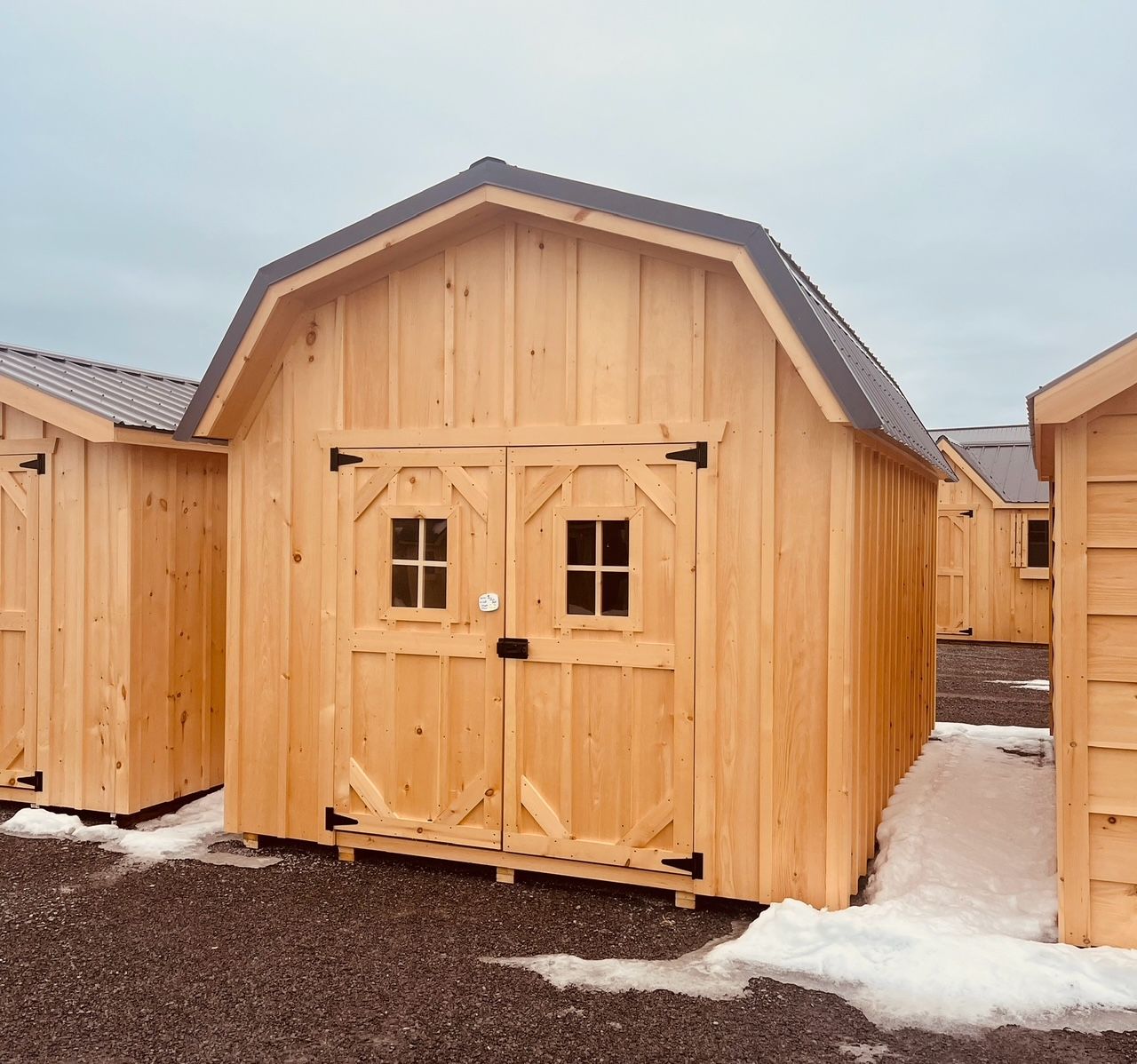 Wooden shed with double doors and windows in a snowy outdoor lot