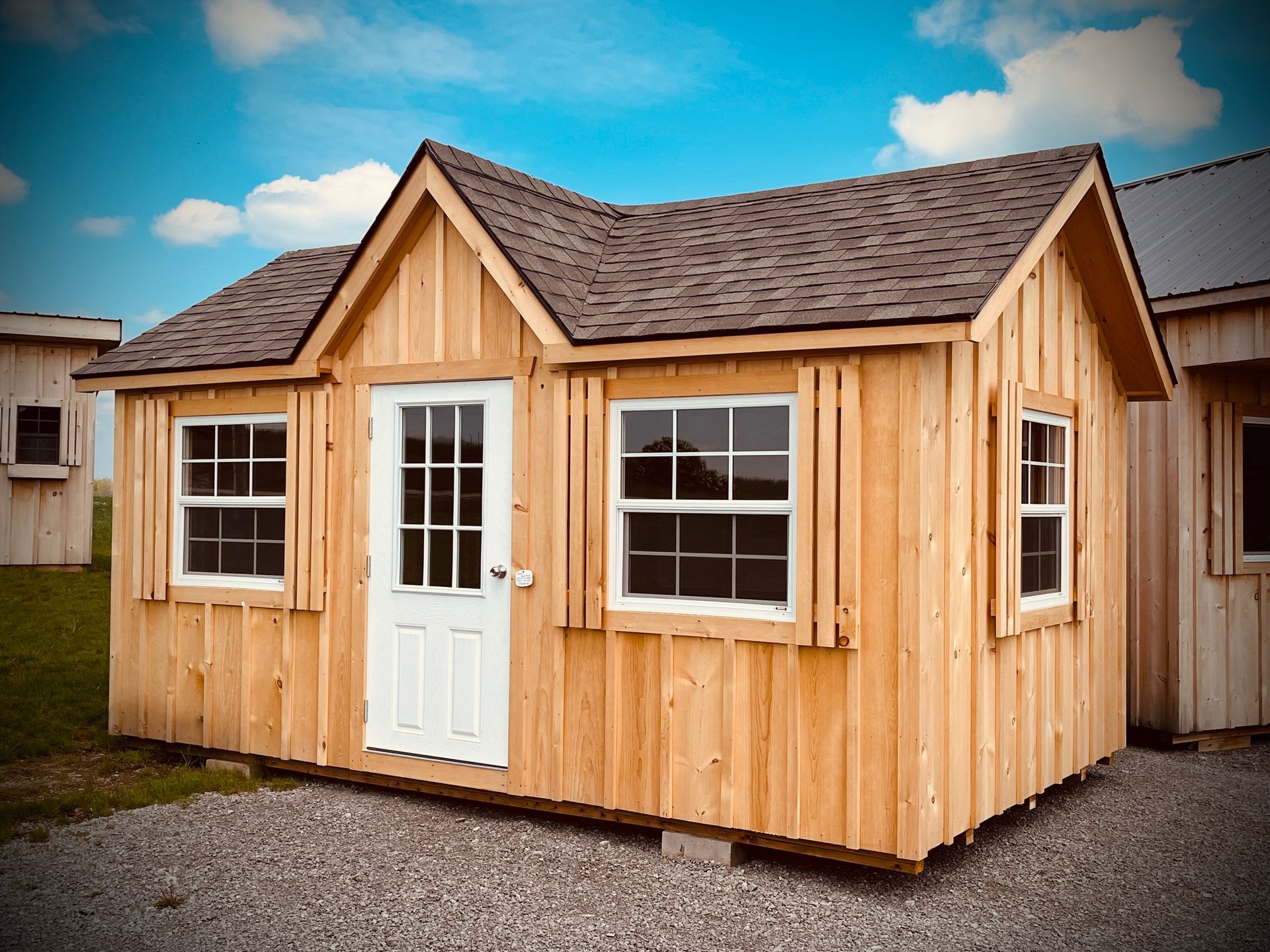A small wooden shed with a roof and windows is sitting on top of a gravel lot.