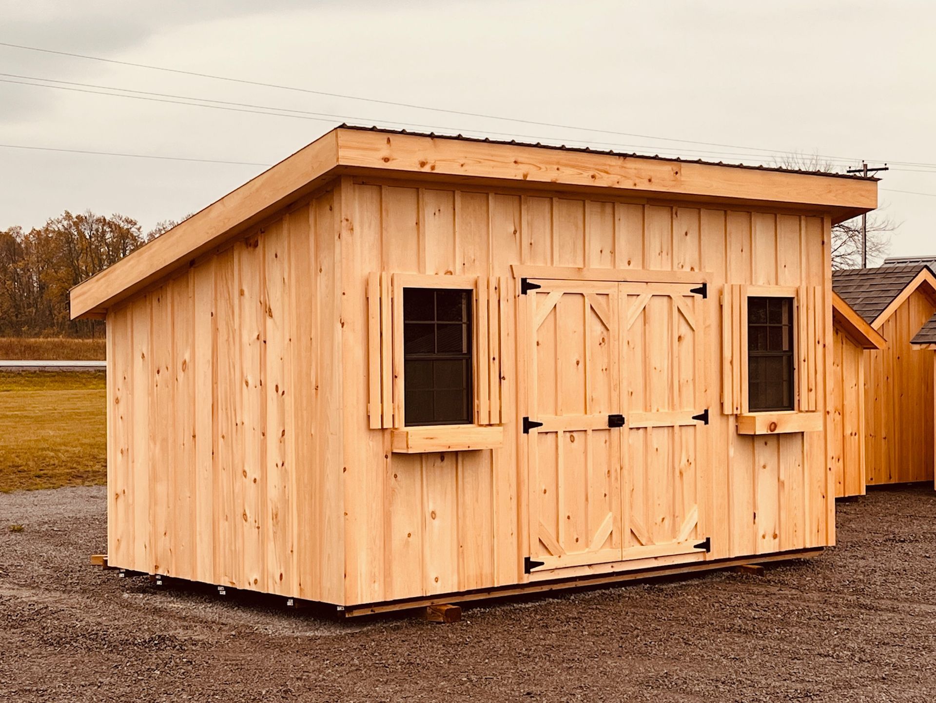 A wooden shed with two windows and a roof is sitting on top of a gravel road.