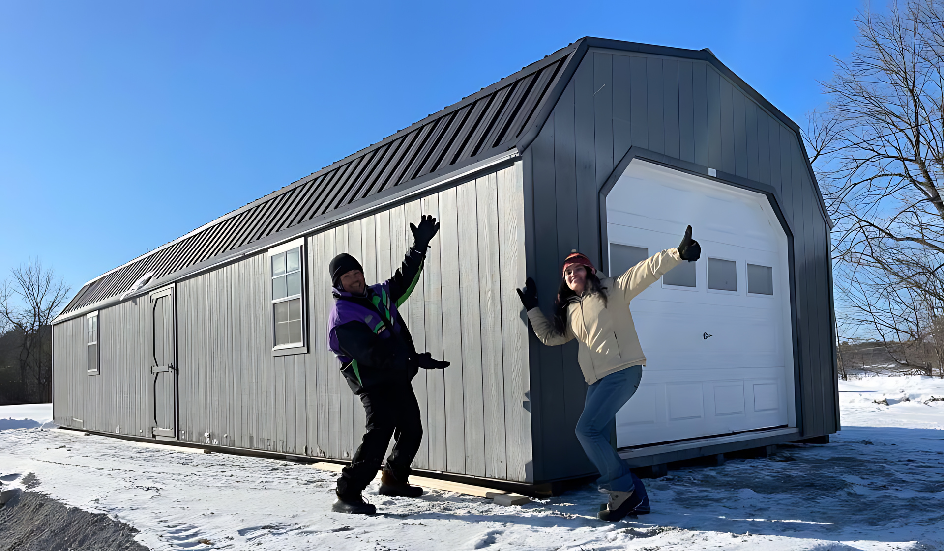 Two people are standing in front of a garage in the snow.