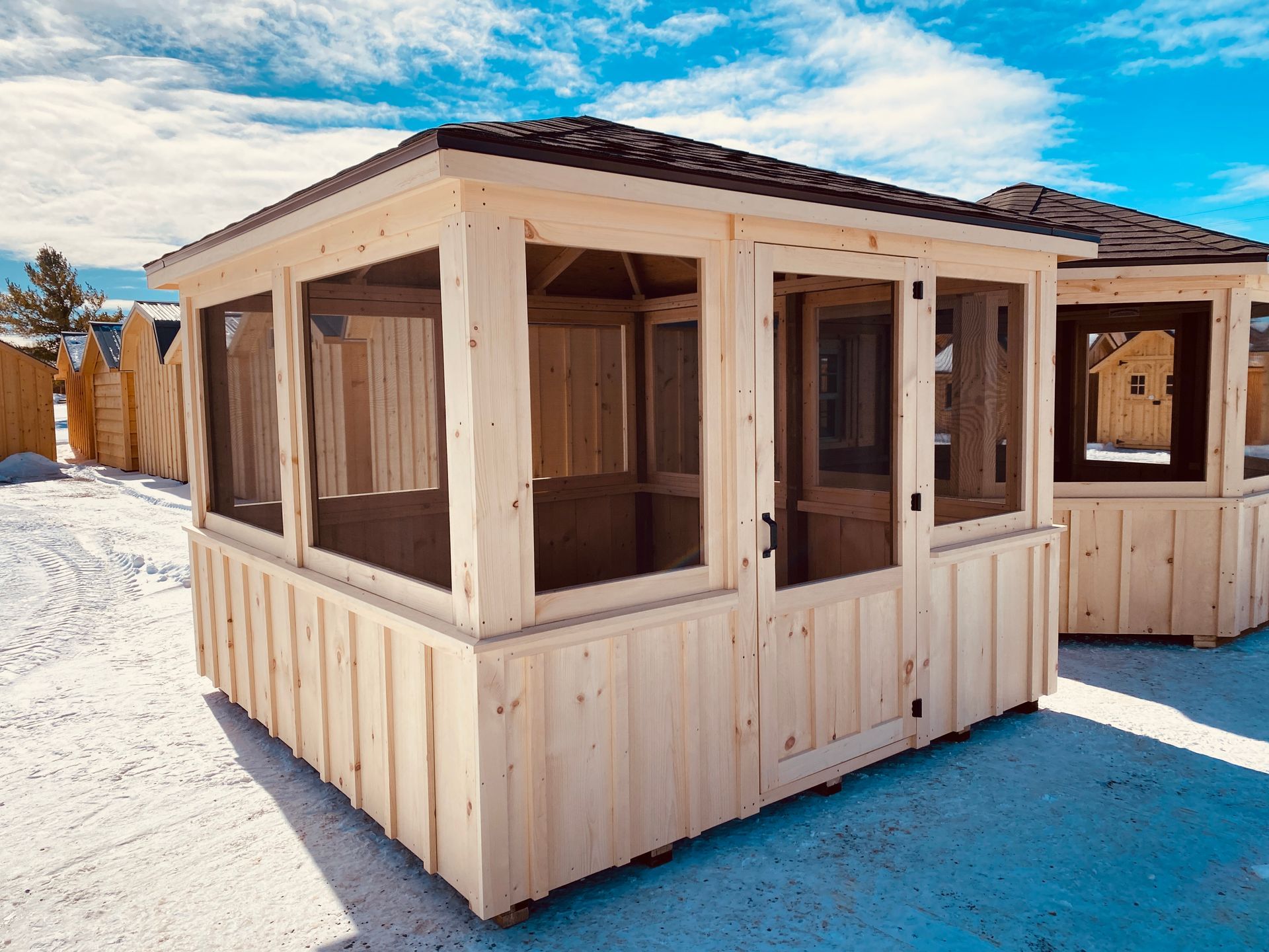 A wooden gazebo with a screened in porch is sitting in the snow.