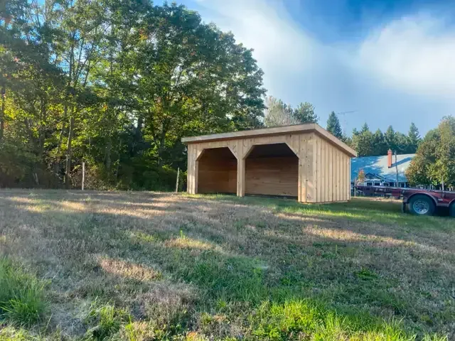 A wooden shed is sitting in the middle of a grassy field.