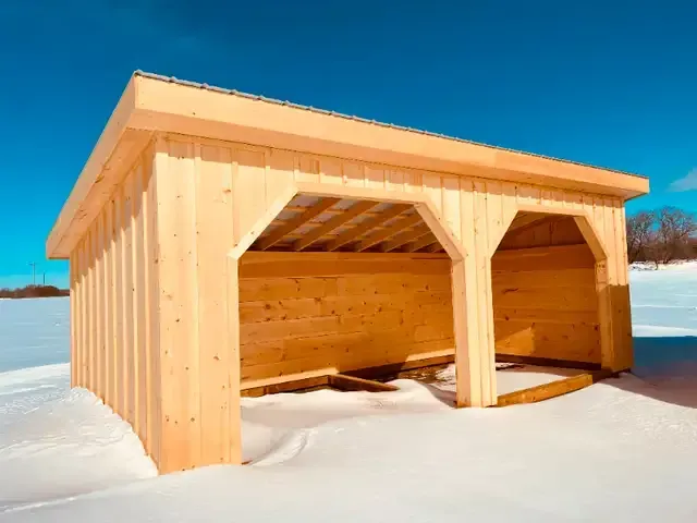 A wooden shelter is sitting in the middle of a snowy field.