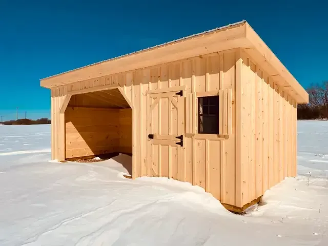 A small wooden shed is sitting in the middle of a snowy field.