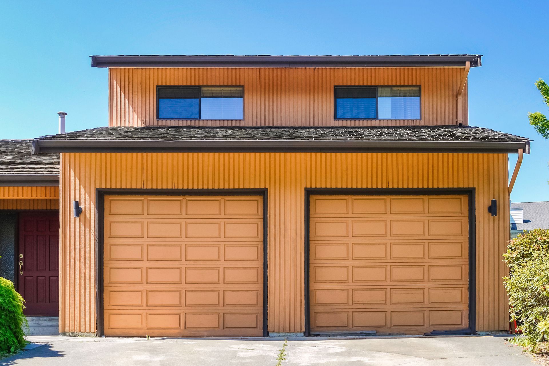 Two-story orange house with two tan garage doors and blue-trimmed windows under a clear sky