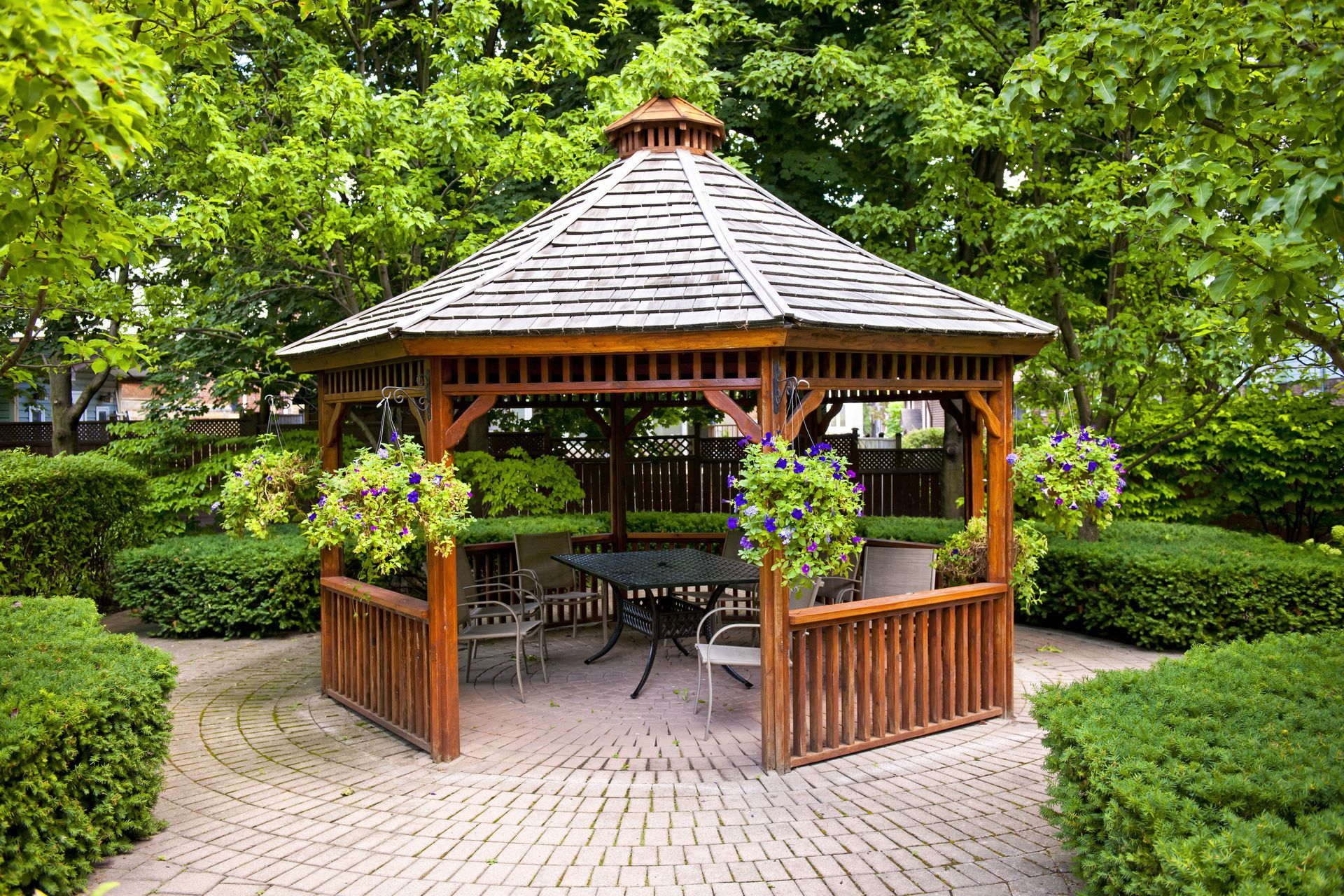 Wooden gazebo with hanging flower baskets in a green park courtyard