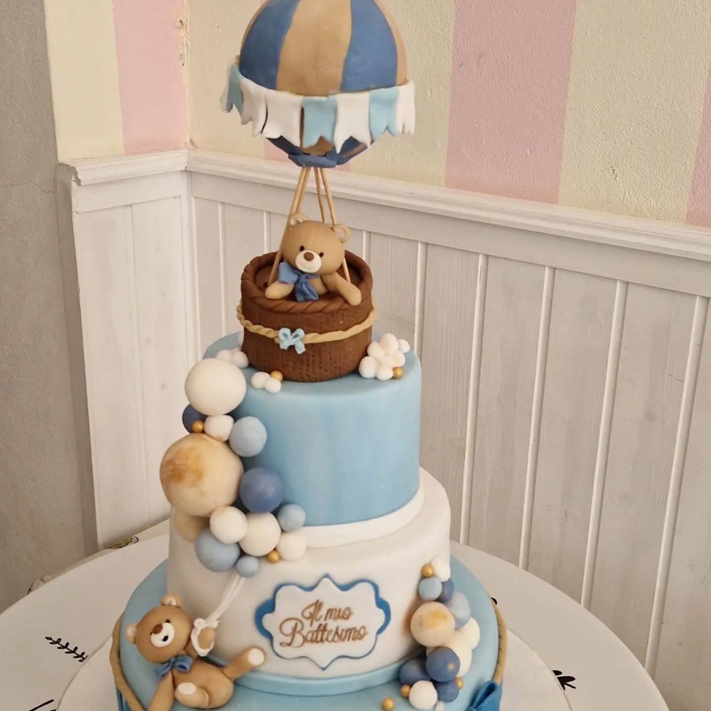 Torta per baby shower a tre piani con una mongolfiera in cima, orsacchiotti e glassa blu e bianca.