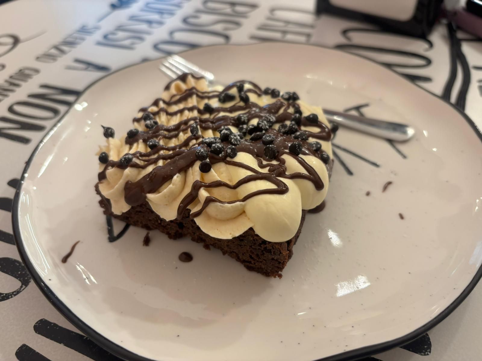 Brownie con panna e gocce di cioccolato su un piatto, con una forchetta a lato.
