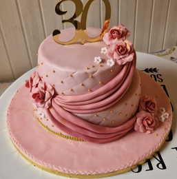 Torta rosa a due piani con glassa di pasta di zucchero, rose, dettagli dorati e una decorazione con la scritta 