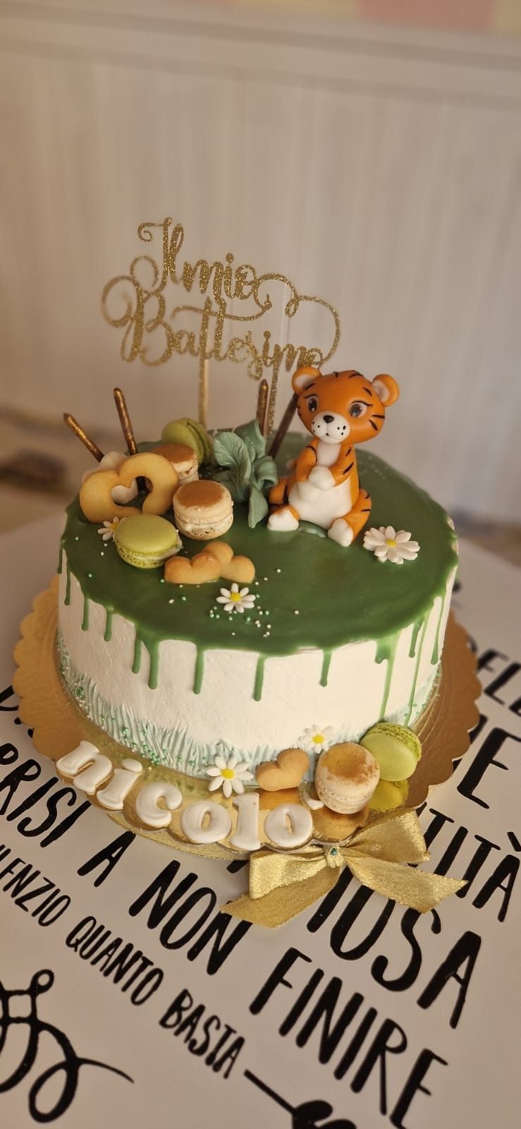 Una torta di compleanno con una statuina di tigre, macaron e il nome "Nicola".