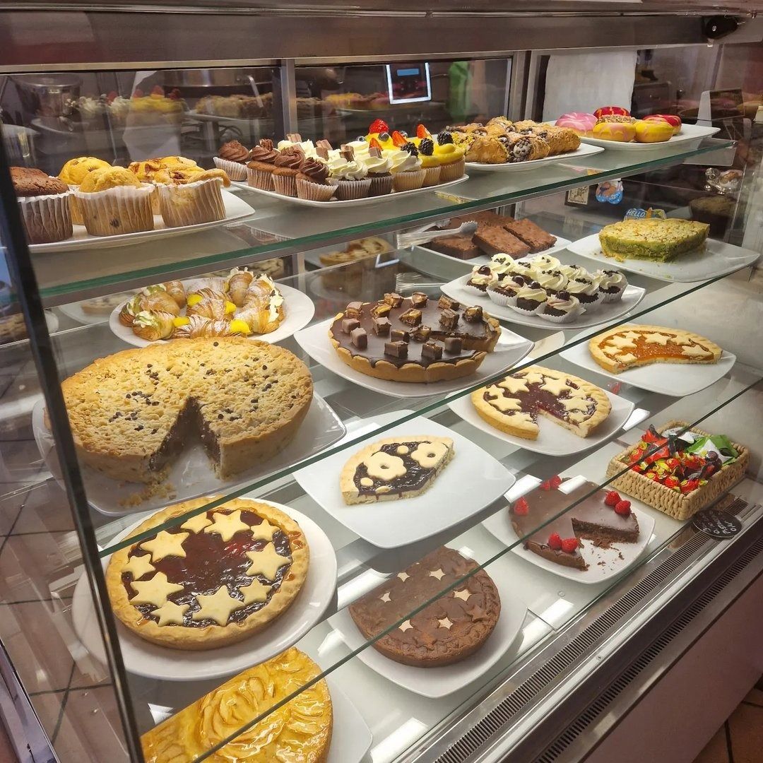 Vetrina con pasticceria assortita, tra cui torte, crostate e muffin, in un ambiente da panetteria.