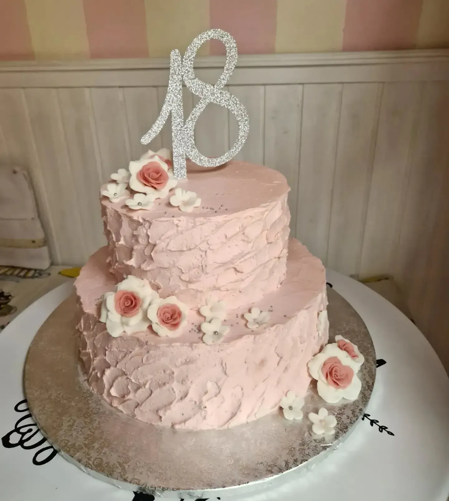 Torta rosa a due piani con decorazioni floreali e una scintillante scritta 