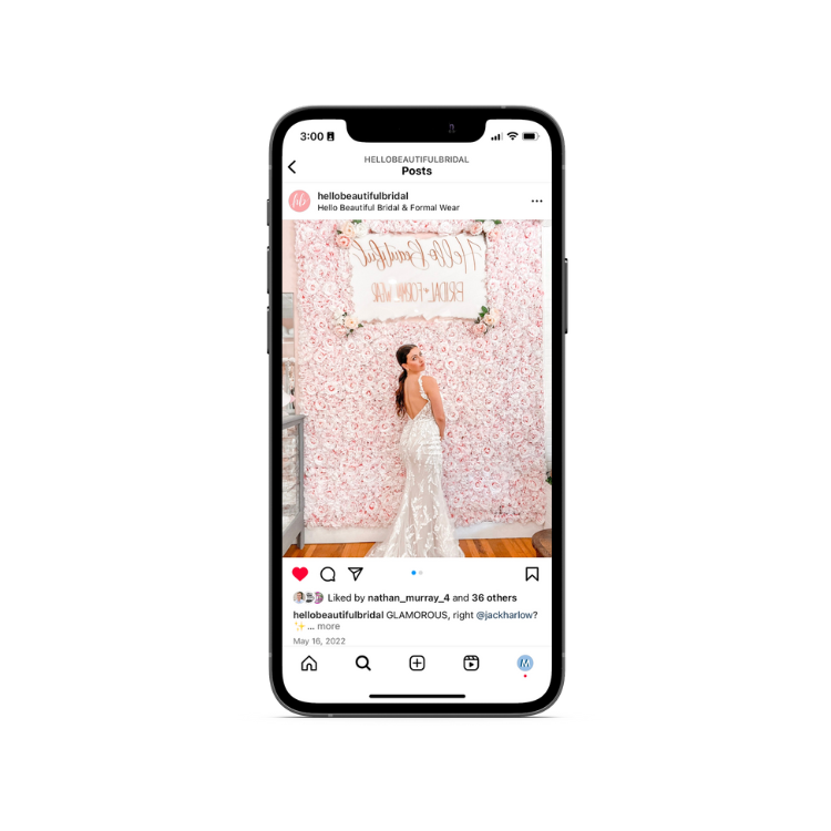 A woman in a wedding dress is standing in front of a flower wall on a cell phone.