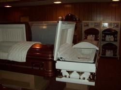 Open casket in a dimly lit funeral home with wood-paneled walls and shelving in the background